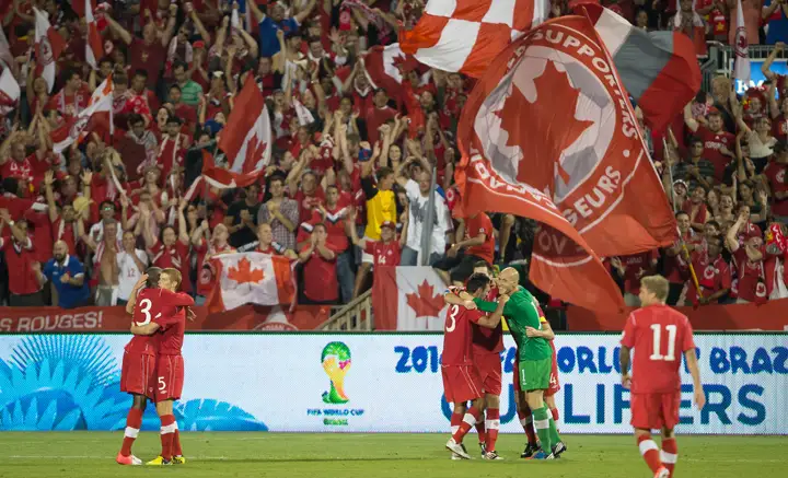 Soccer players celebrate with cheering Canadian fans.