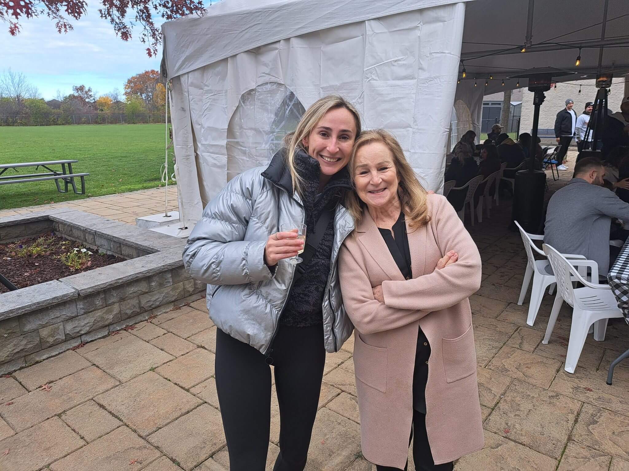 Two women smiling outdoors, one holding a drink.
