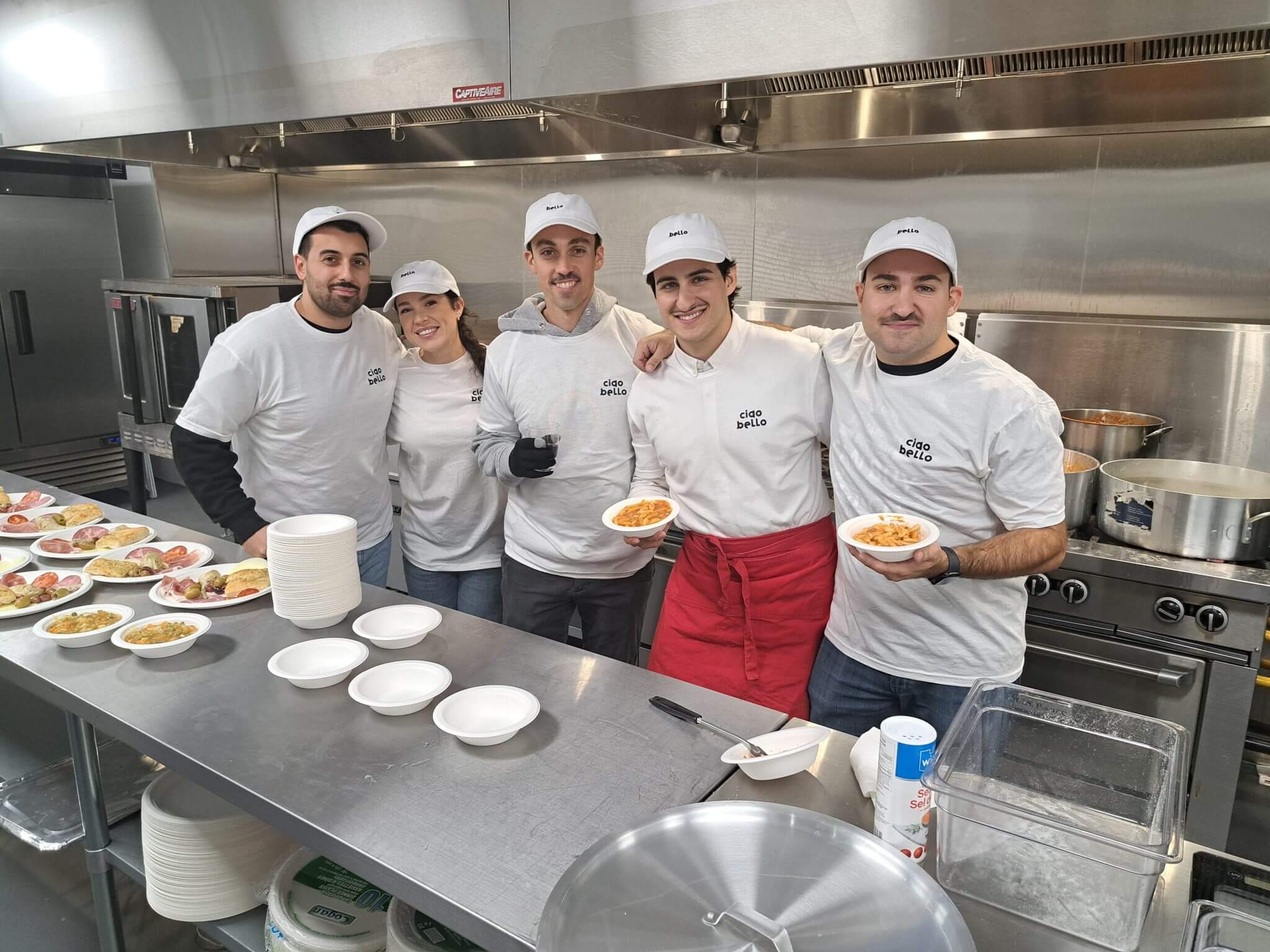 Group of chefs posing in a commercial kitchen holding plates of food.