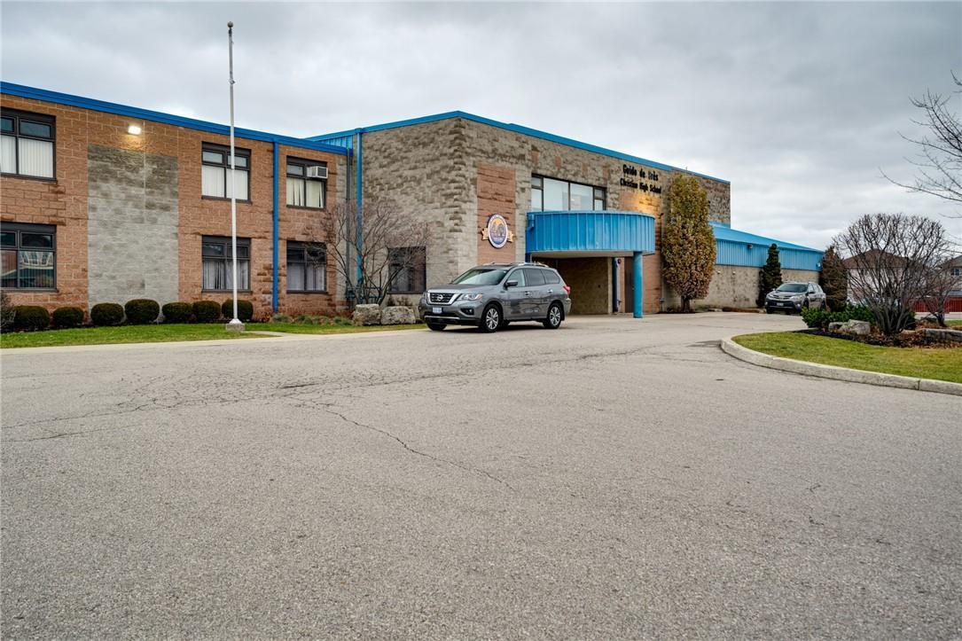 A black car parked outside a brick and blue school building under a cloudy sky.