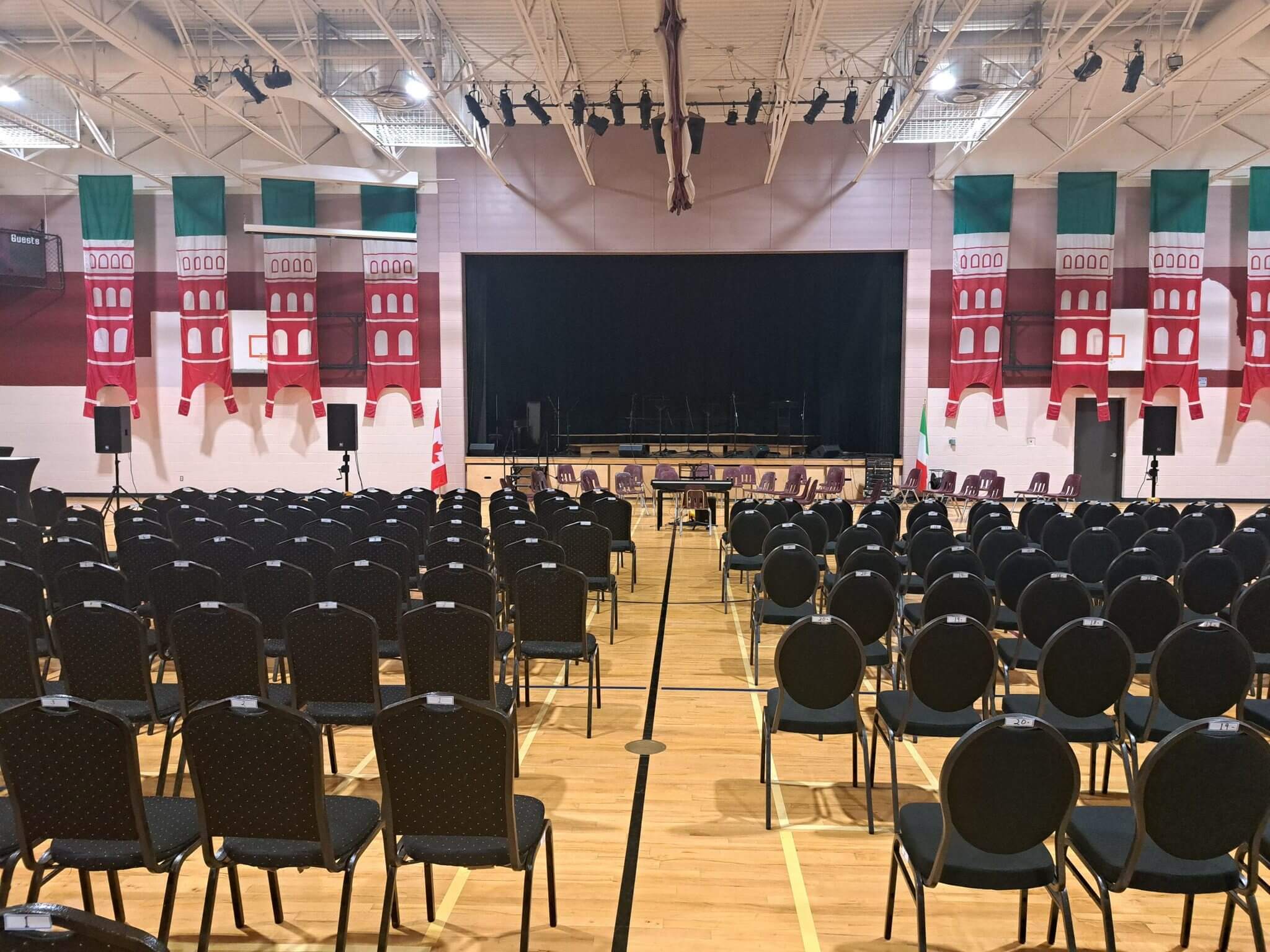 Empty gymnasium set up for an event with a stage and rows of chairs.