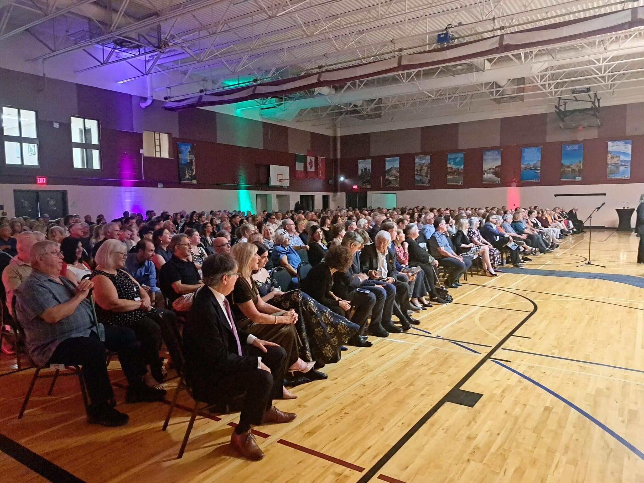 Audience attentively watching an event in a gymnasium with colorful lighting.