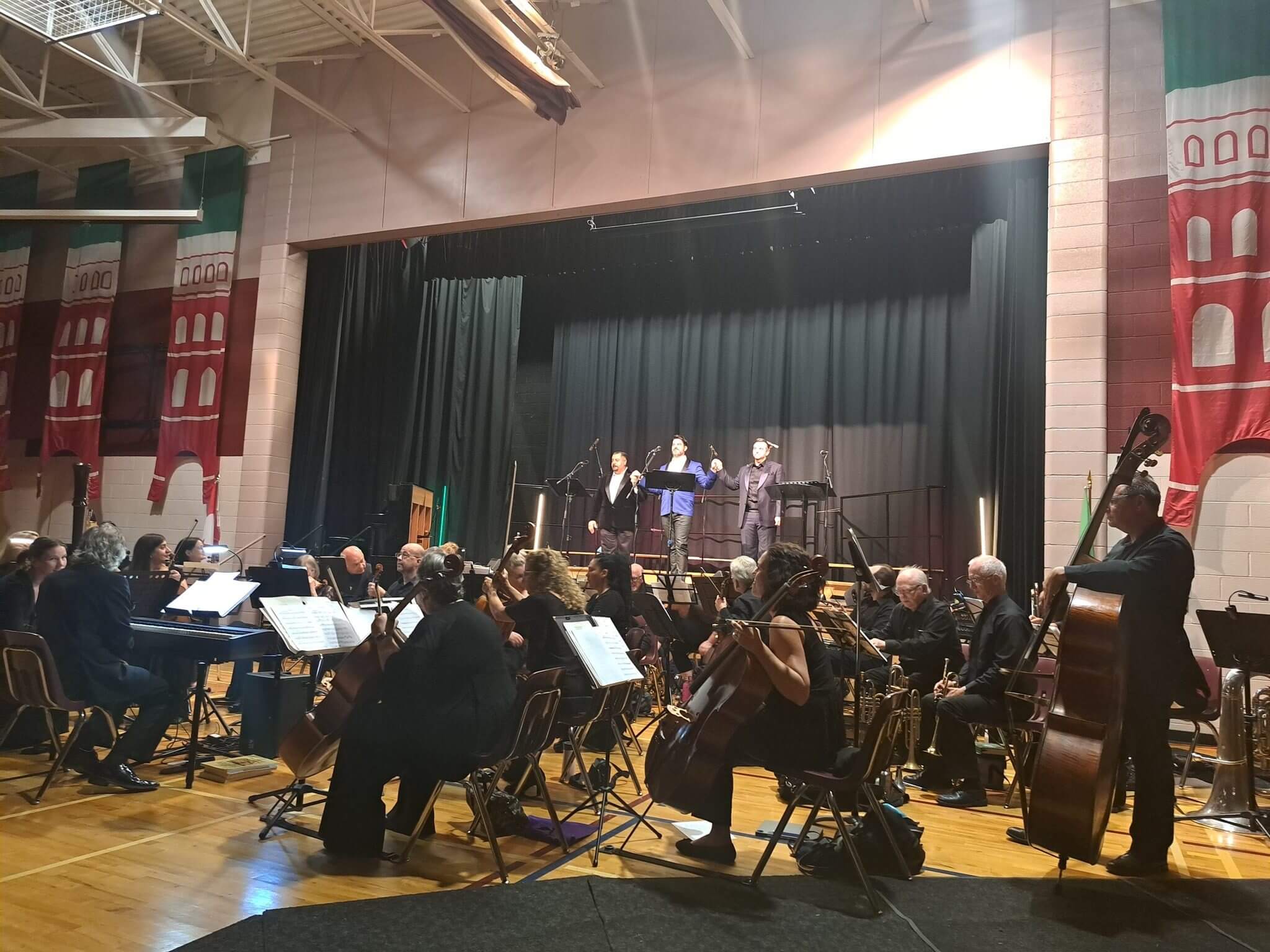 An orchestra performs on stage in a gymnasium with a conductor leading.