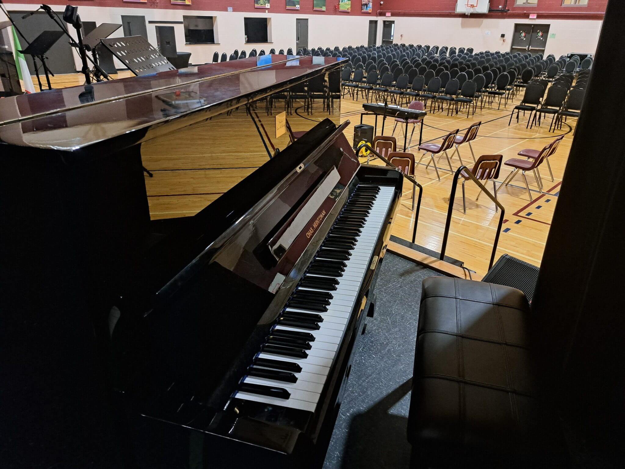 A piano on a stage overlooking empty chairs in an auditorium.