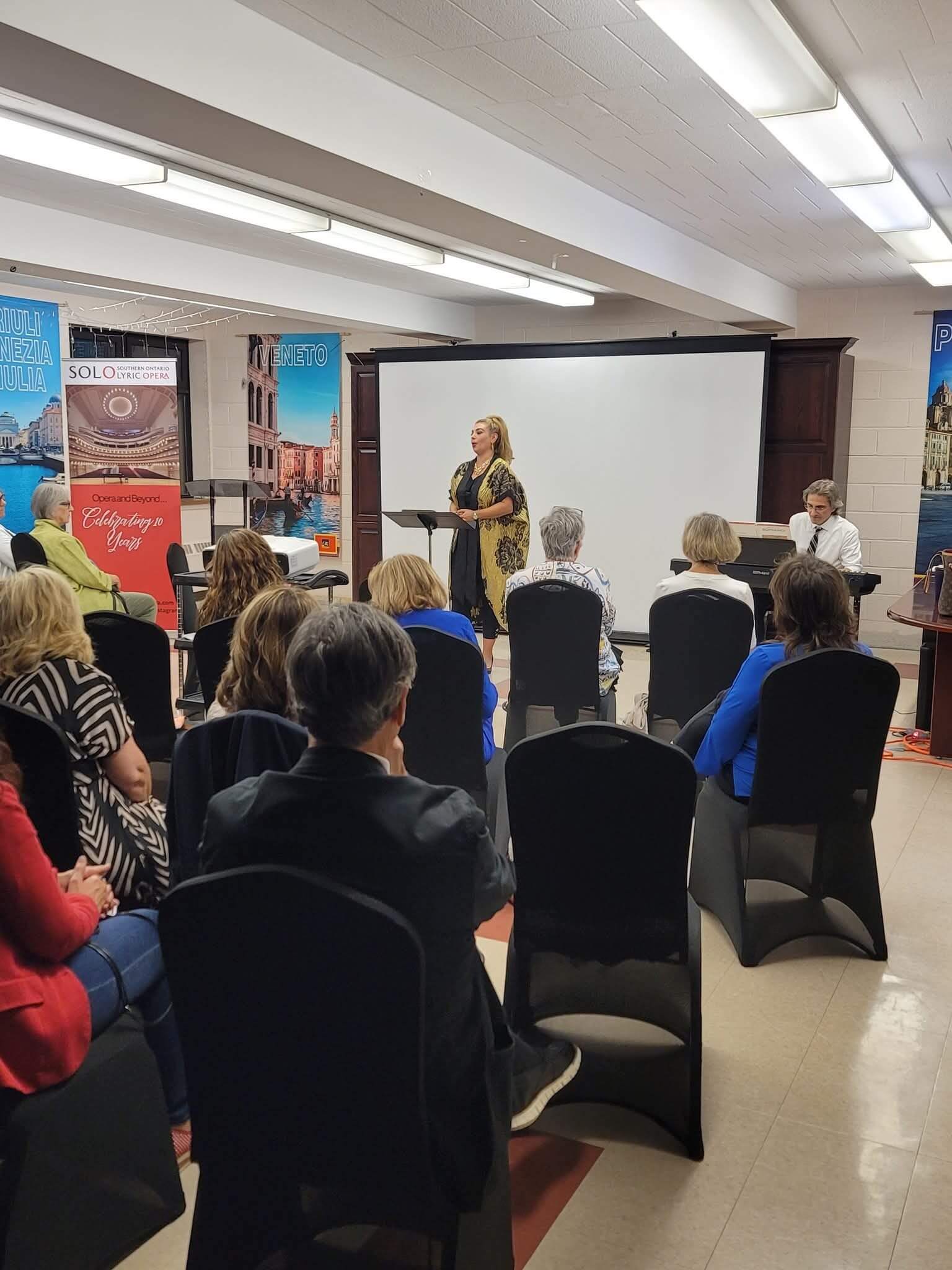A woman speaks to an audience seated in a conference room.