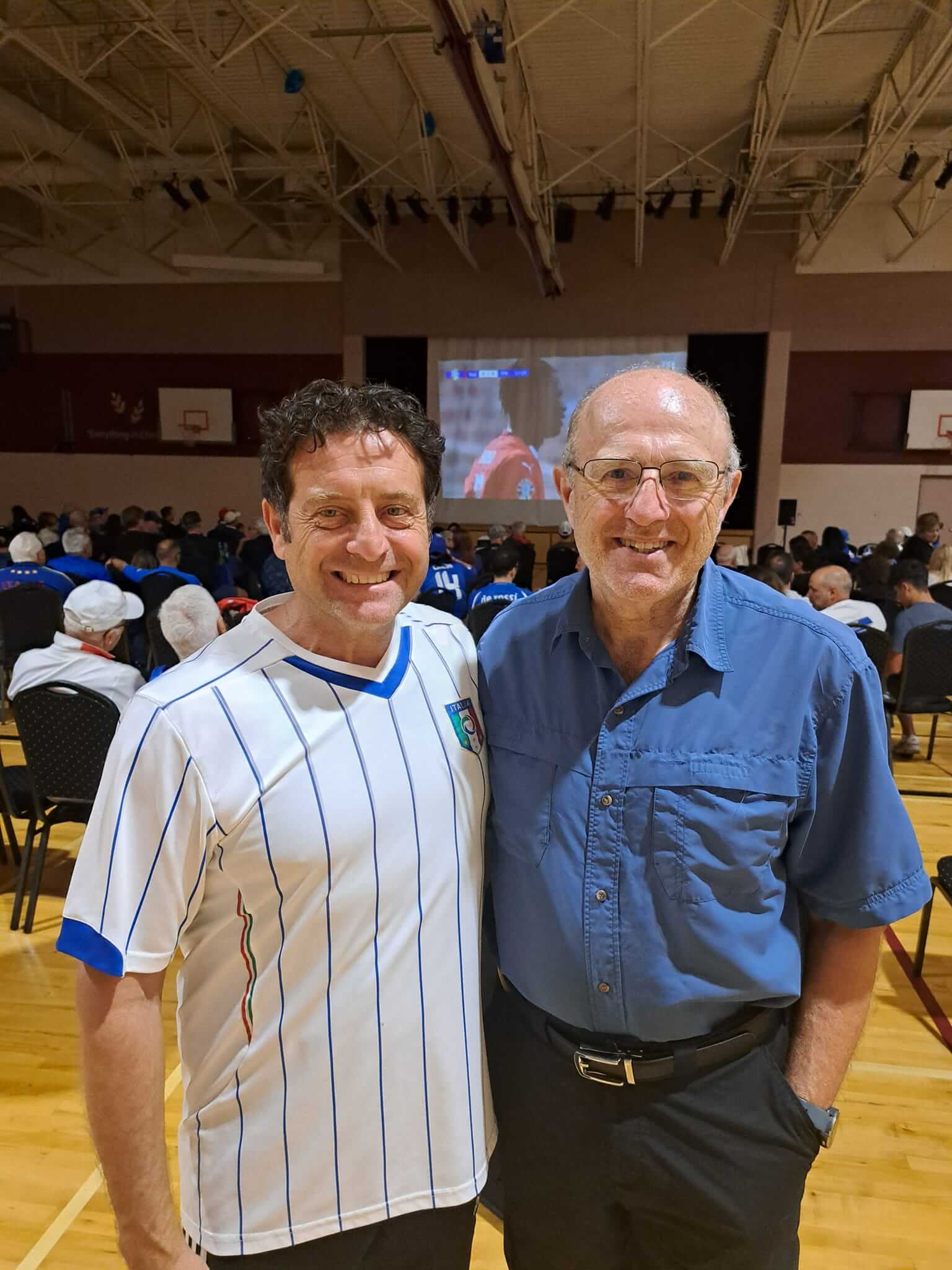 Two men smiling together in a gymnasium setting.