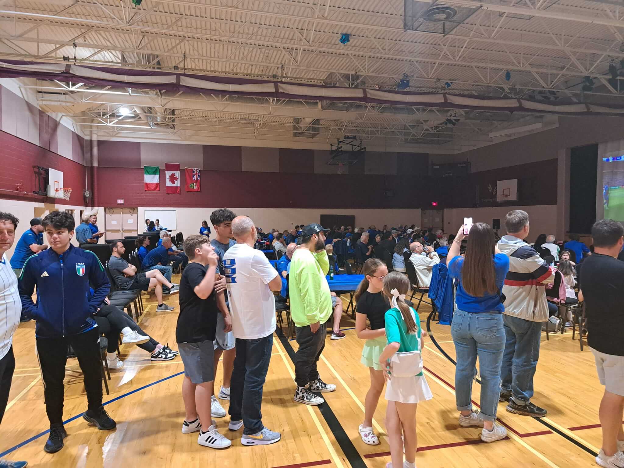 People gathering indoors in a gymnasium, some wearing masks.