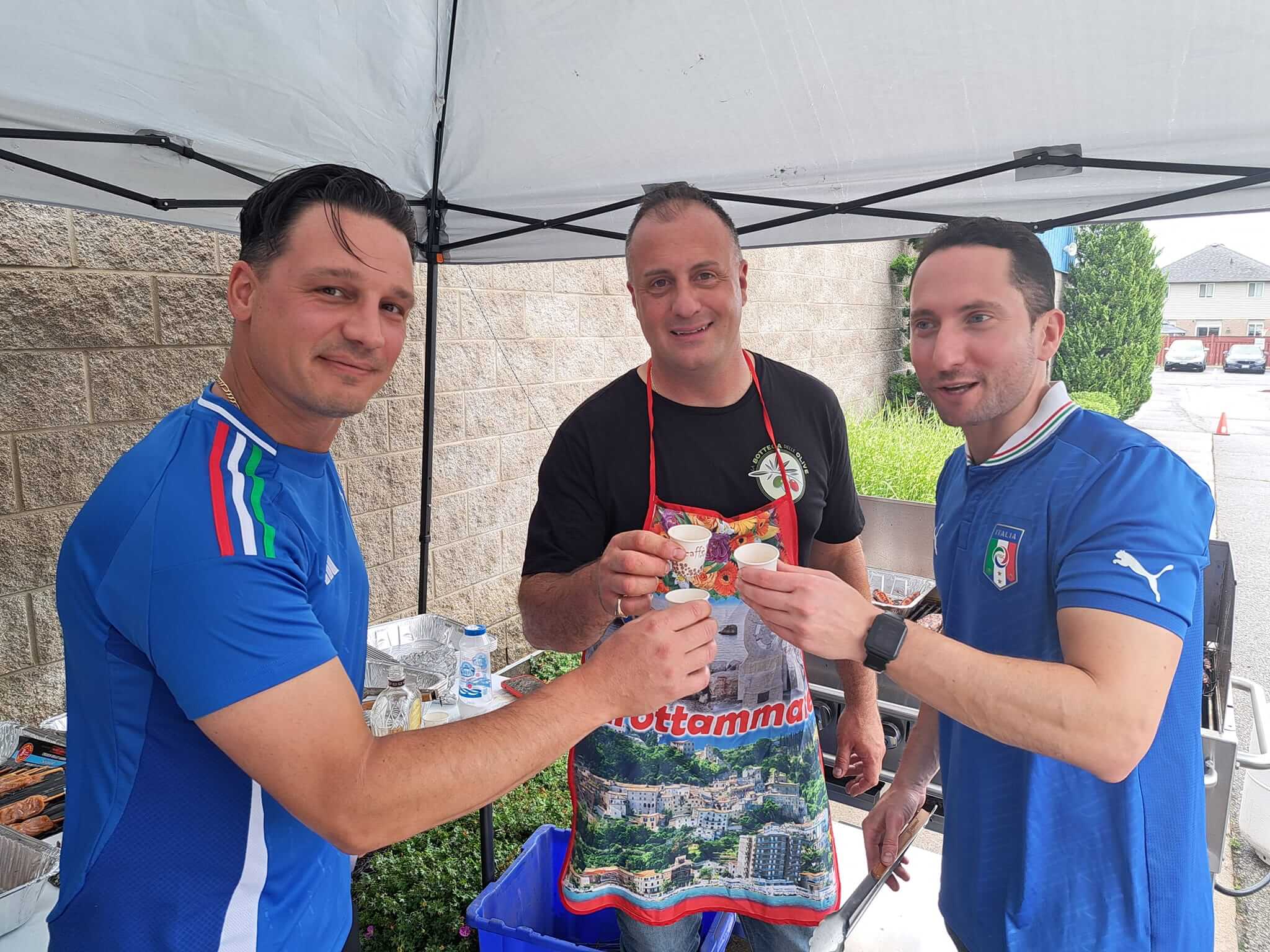 Three men in sports jerseys enjoying drinks under a canopy.