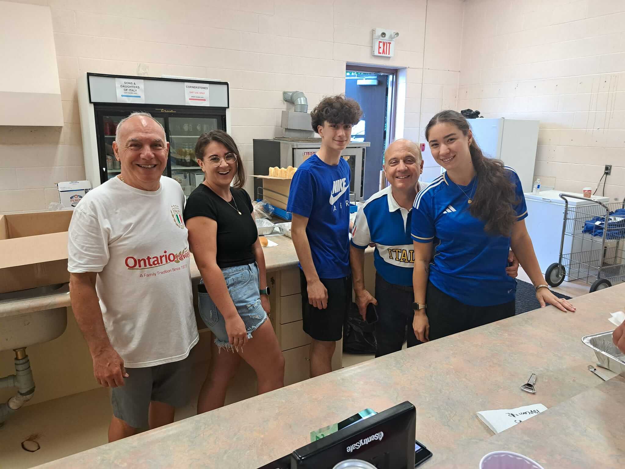 Group of six people smiling and posing in a kitchen setting.