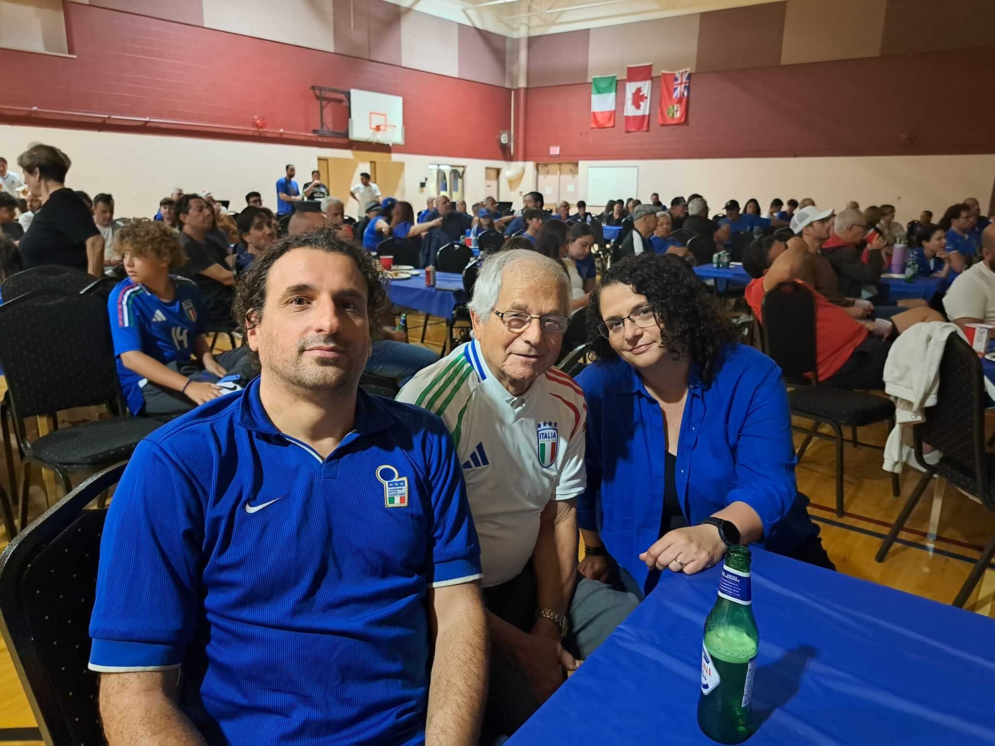 Three people smiling at a crowded indoor event with flags and decorations.