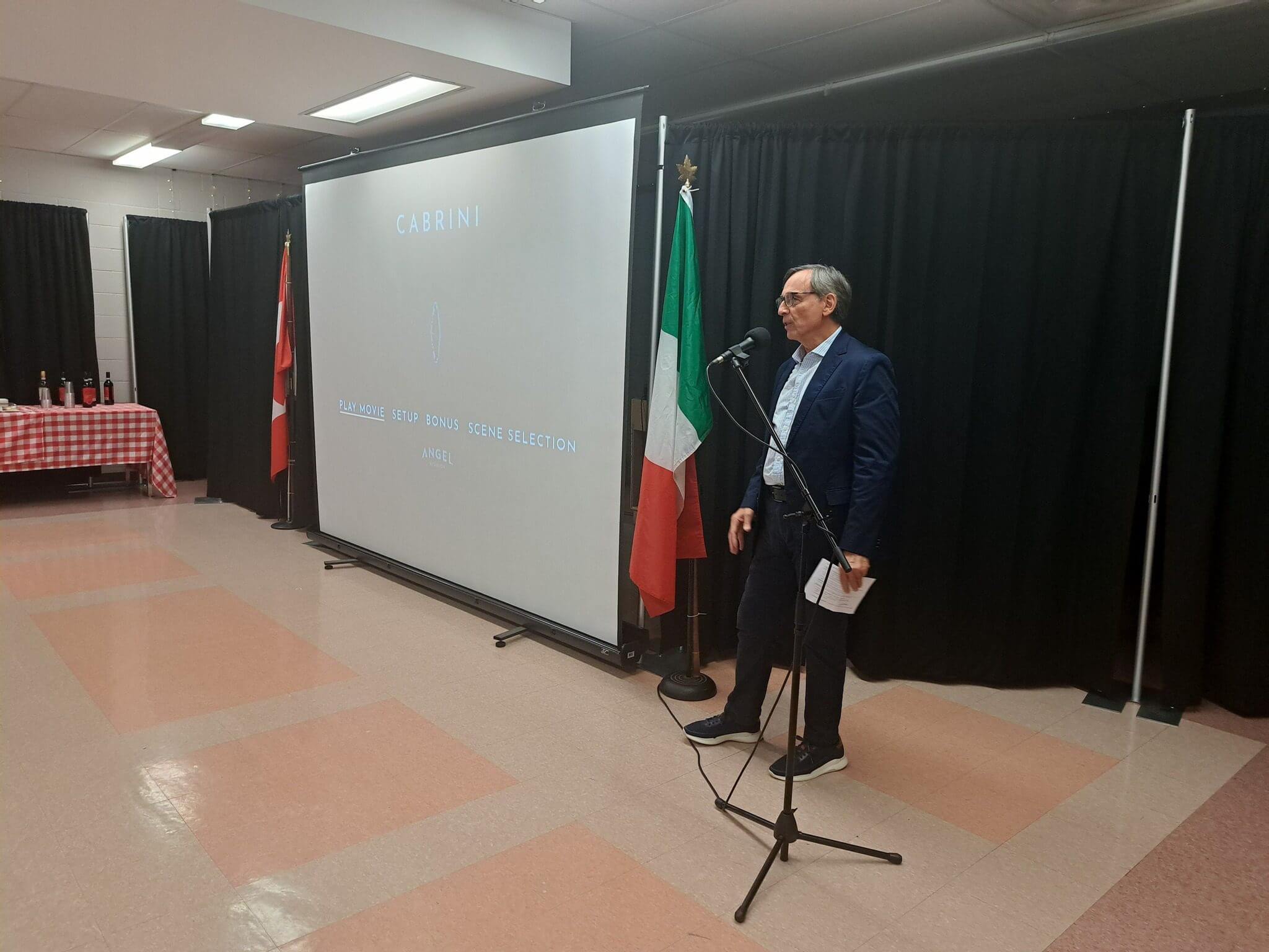 Man speaking at a podium with Italian and Albanian flags behind.