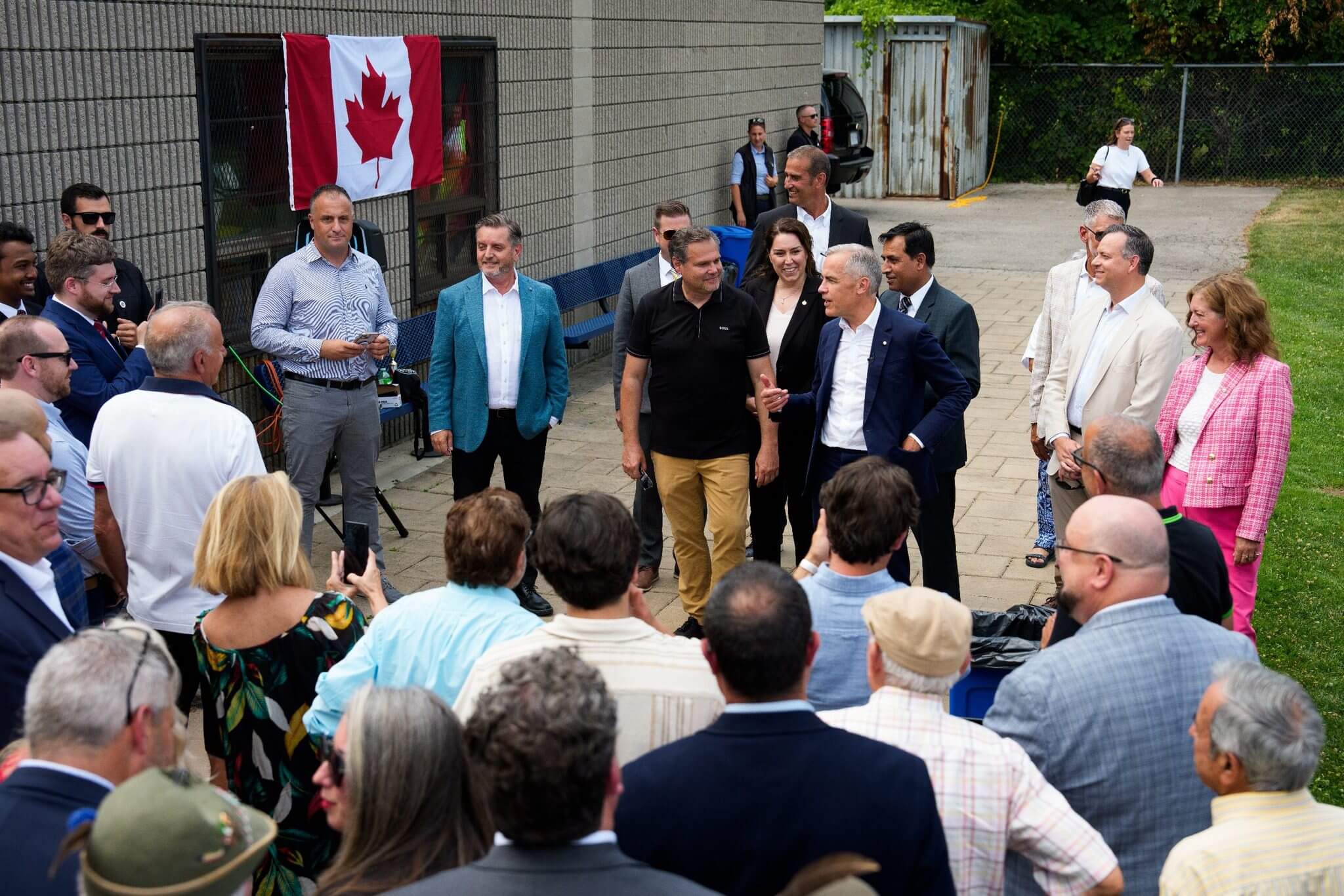 A group of people gathered outdoors near a Canadian flag, engaged in conversation.