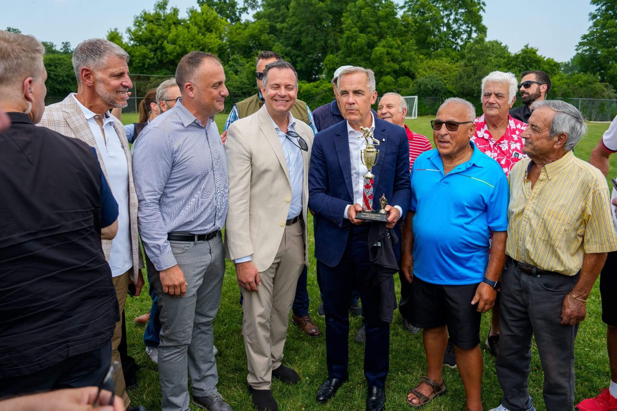 A group of men posing outdoors, one holding a trophy.