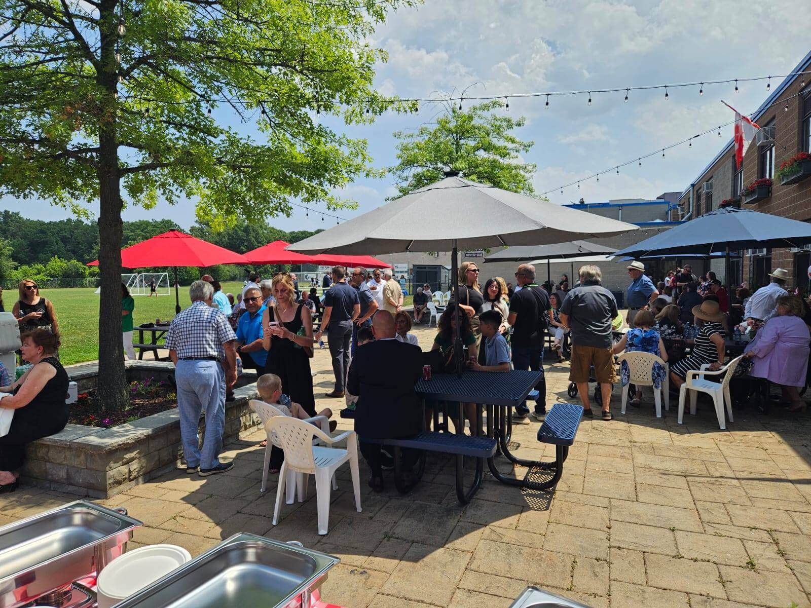 People gather under umbrellas enjoying an outdoor event on a sunny day.