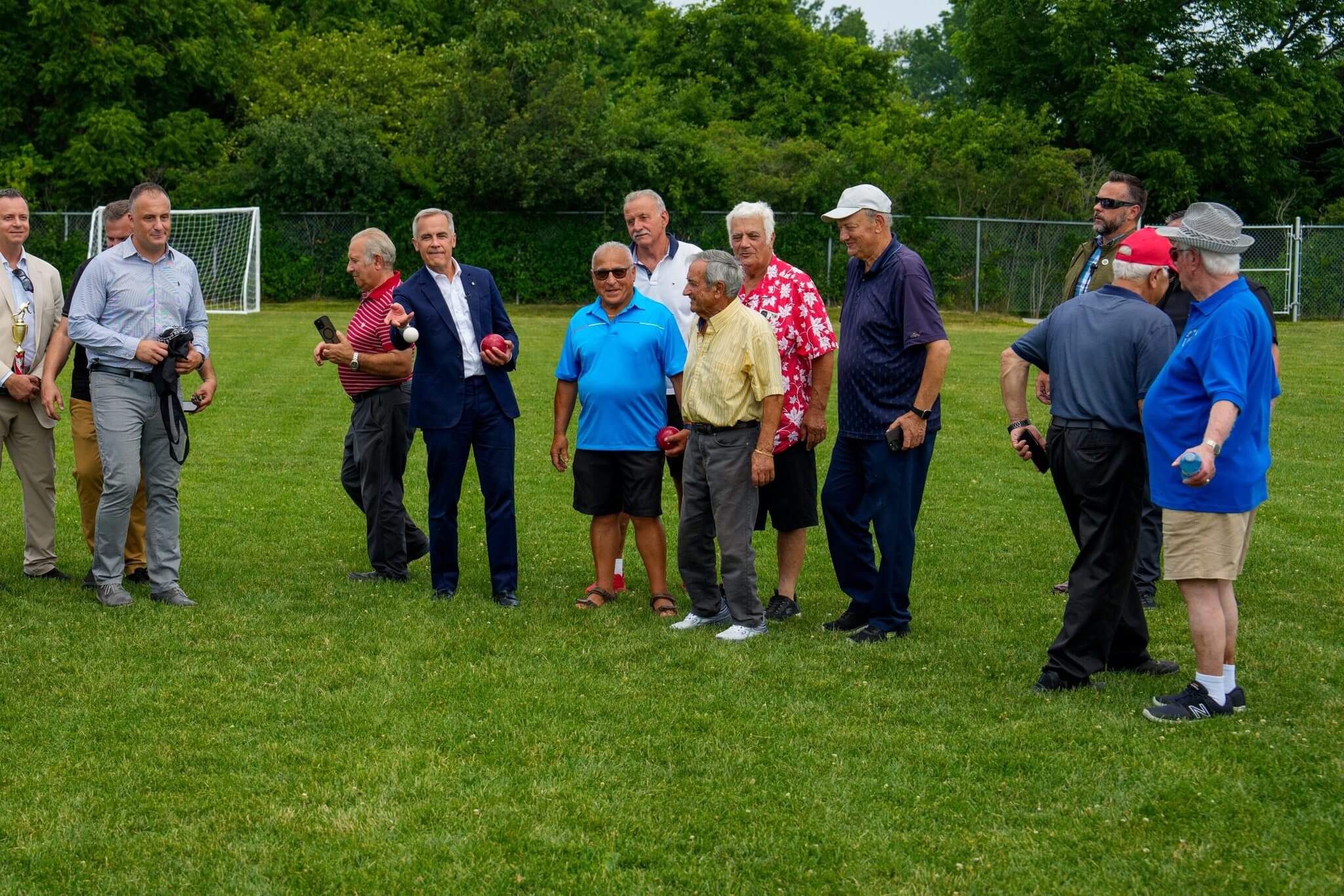 Group of people standing on a grassy field with a soccer goal in the background.