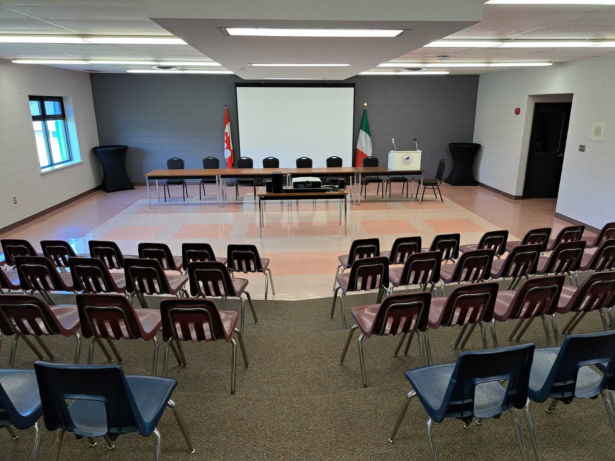 Empty conference room with rows of chairs facing a projection screen.