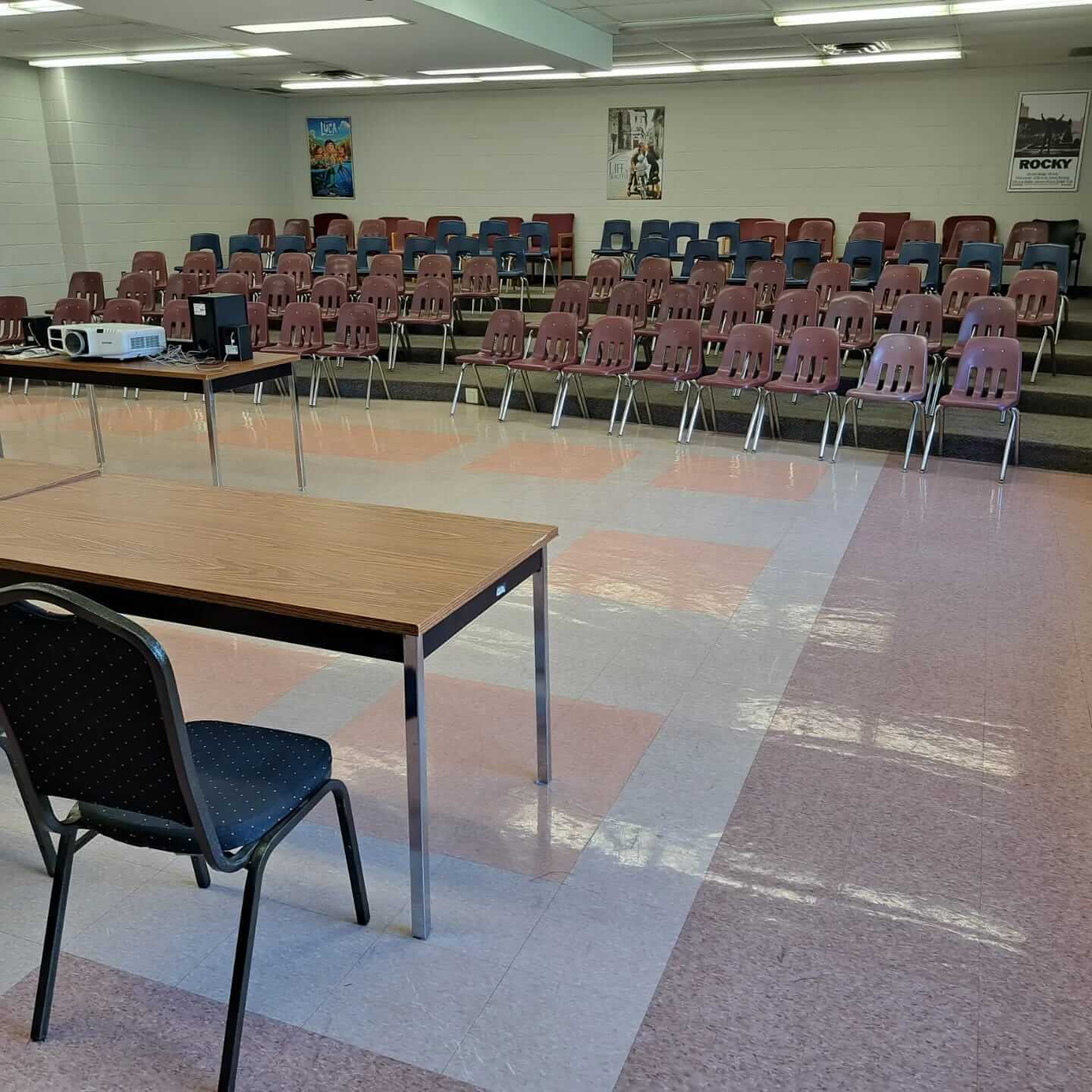 Empty room with rows of chairs and microphone stands, set for an event or presentation.
