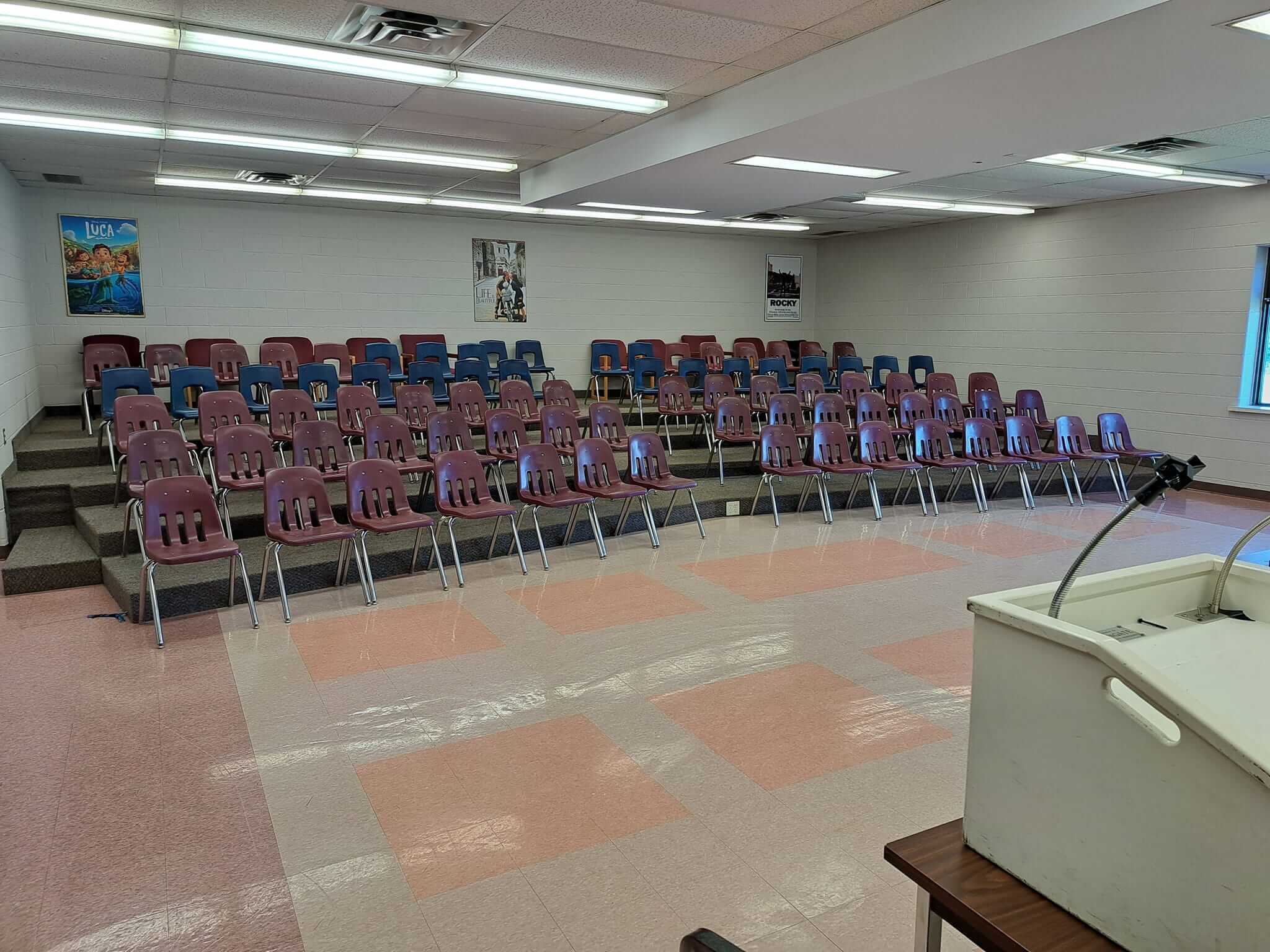 Empty lecture hall with rows of chairs and a podium.