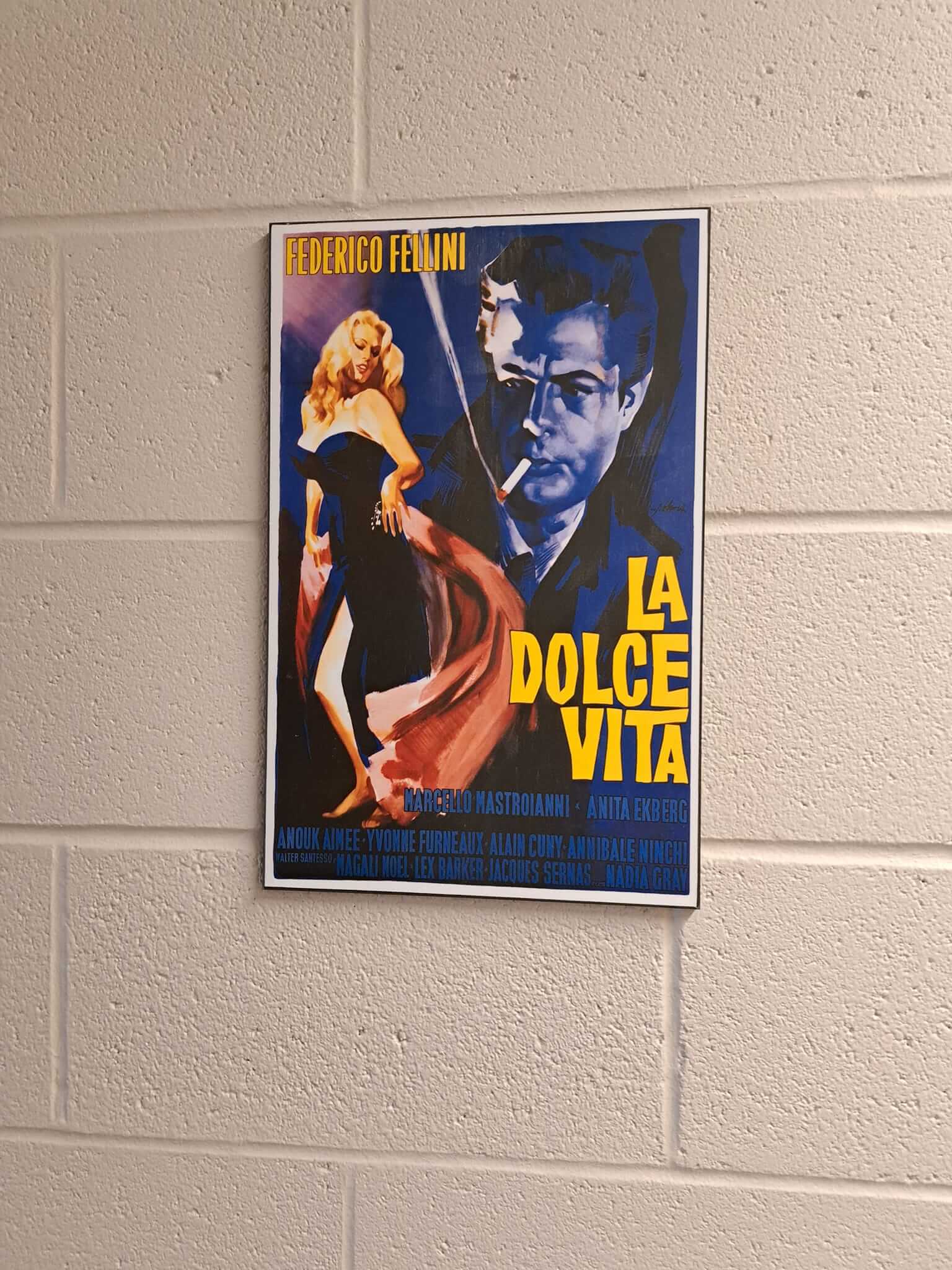 Retro movie poster for 'La Dolce Vita' with bold colors on a brick wall.