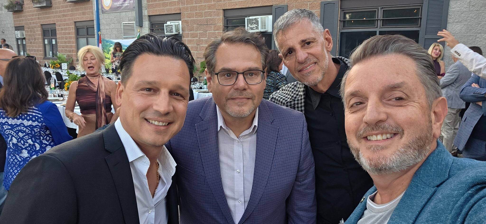 Four men posing for a group selfie outdoors.