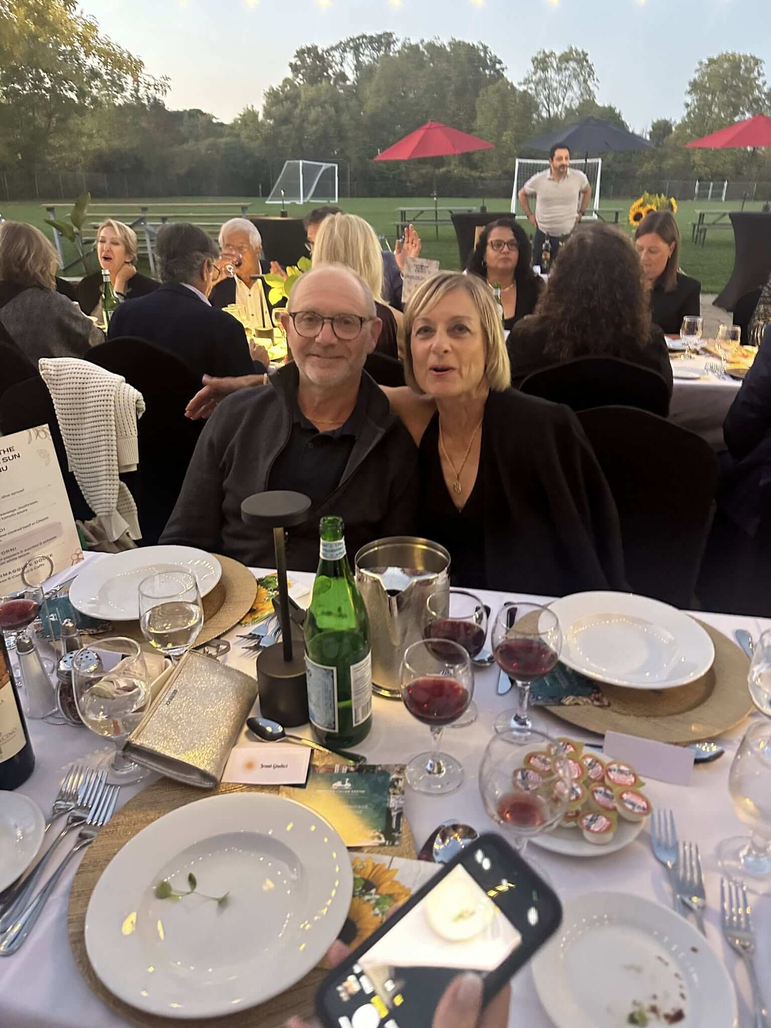Two women smiling at an outdoor dinner party with drinks and food on the table.