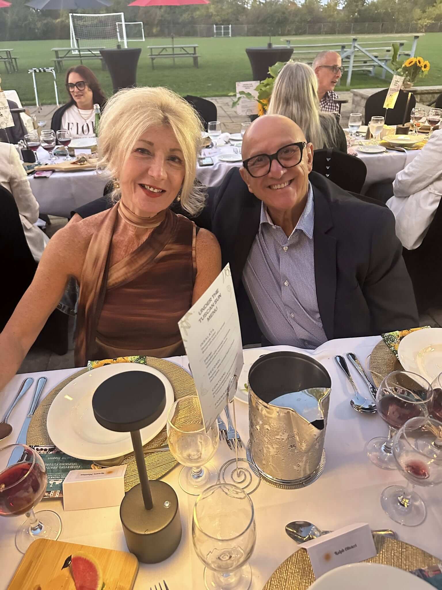 Elderly couple smiling at a formal dining event with elegant table settings.
