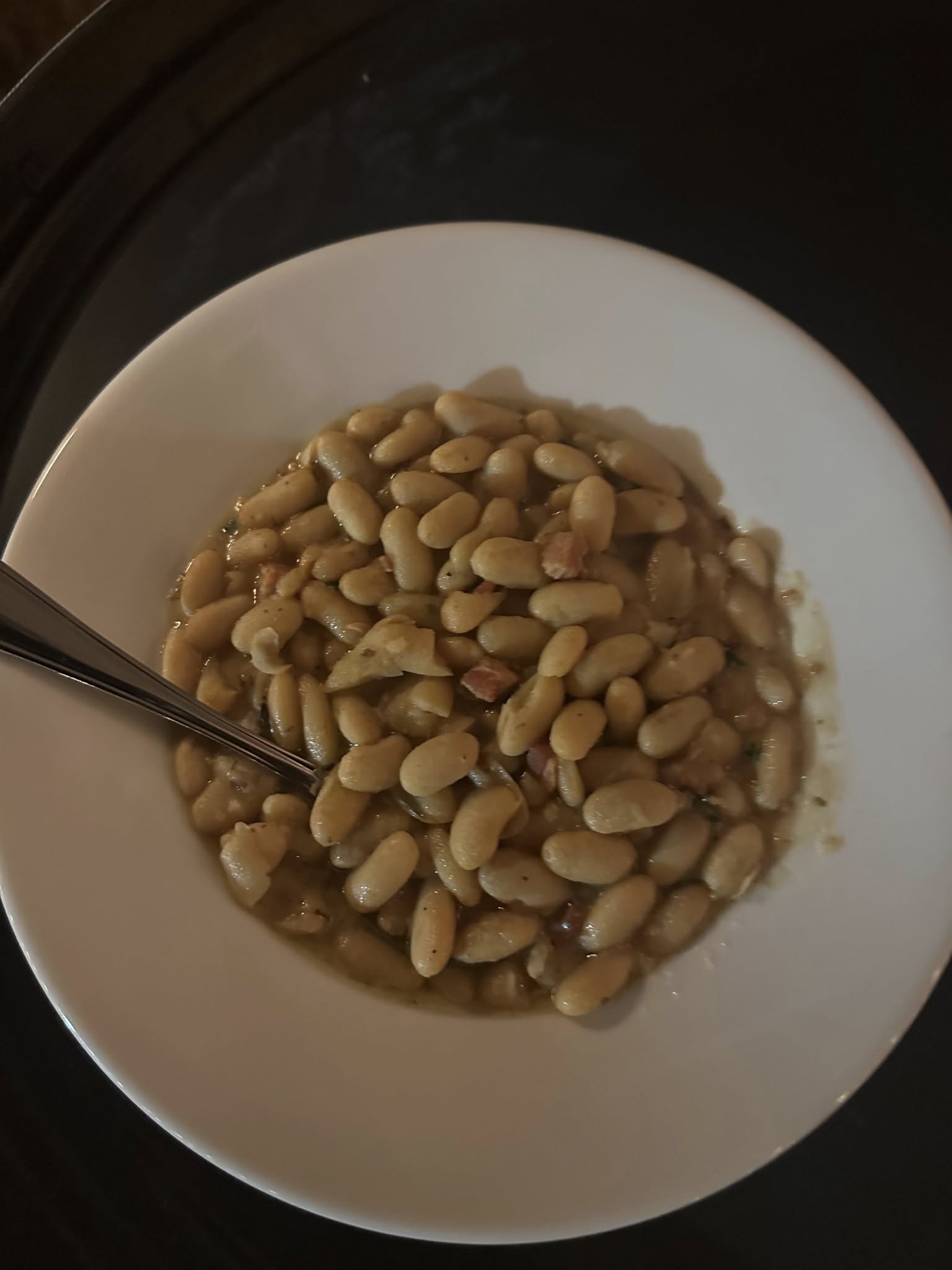 A bowl of cooked white beans with a spoon.