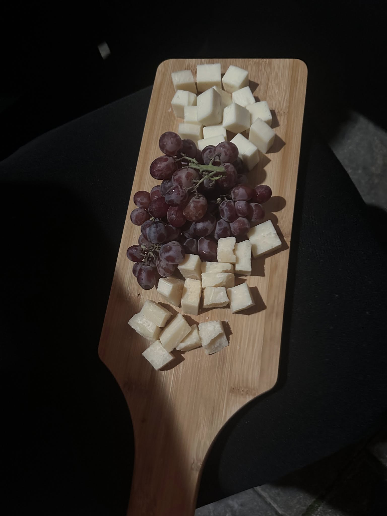 Cheese cubes and red grapes arranged on a wooden board.