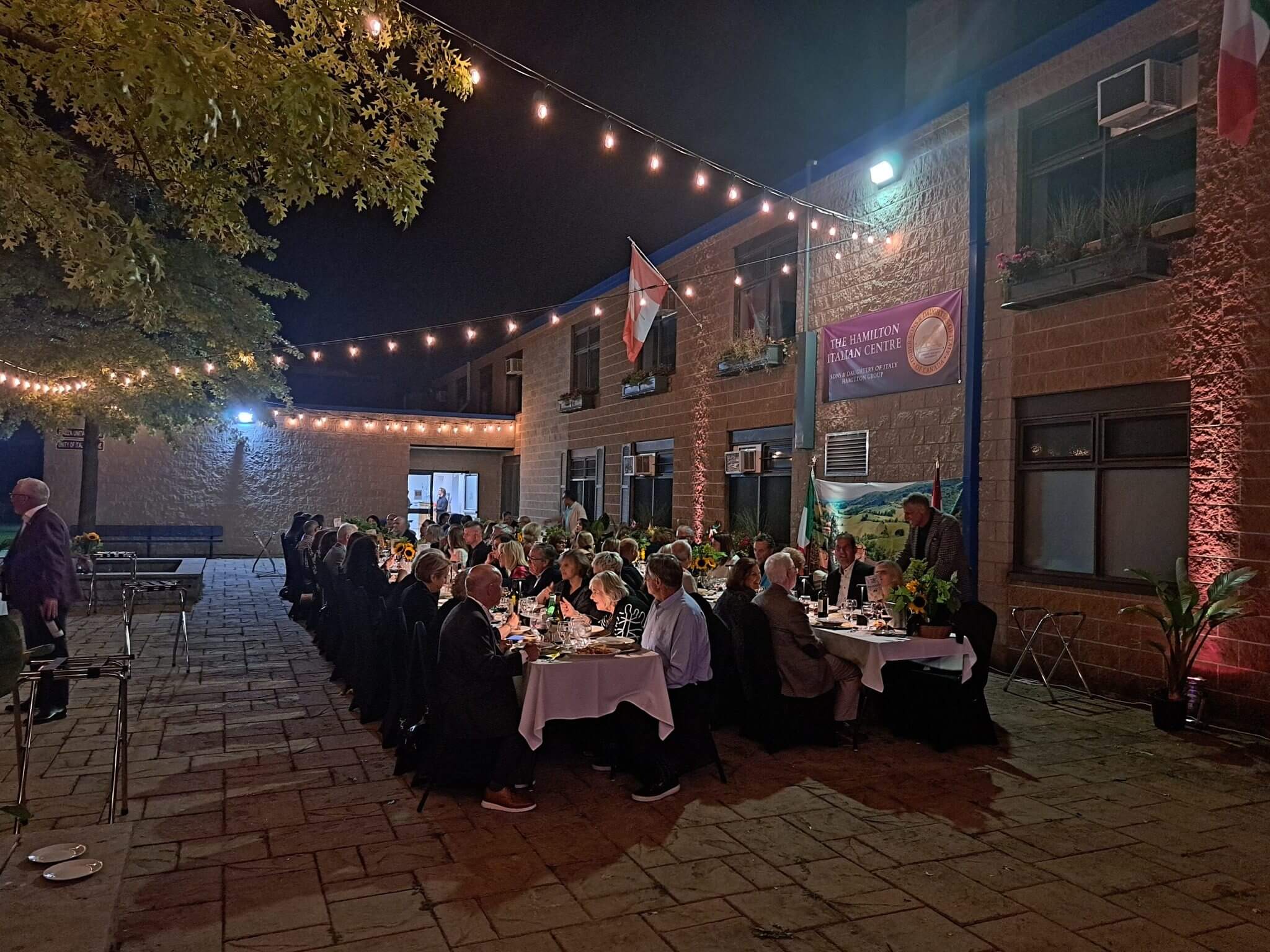 Outdoor nighttime gathering with string lights and long dining tables.