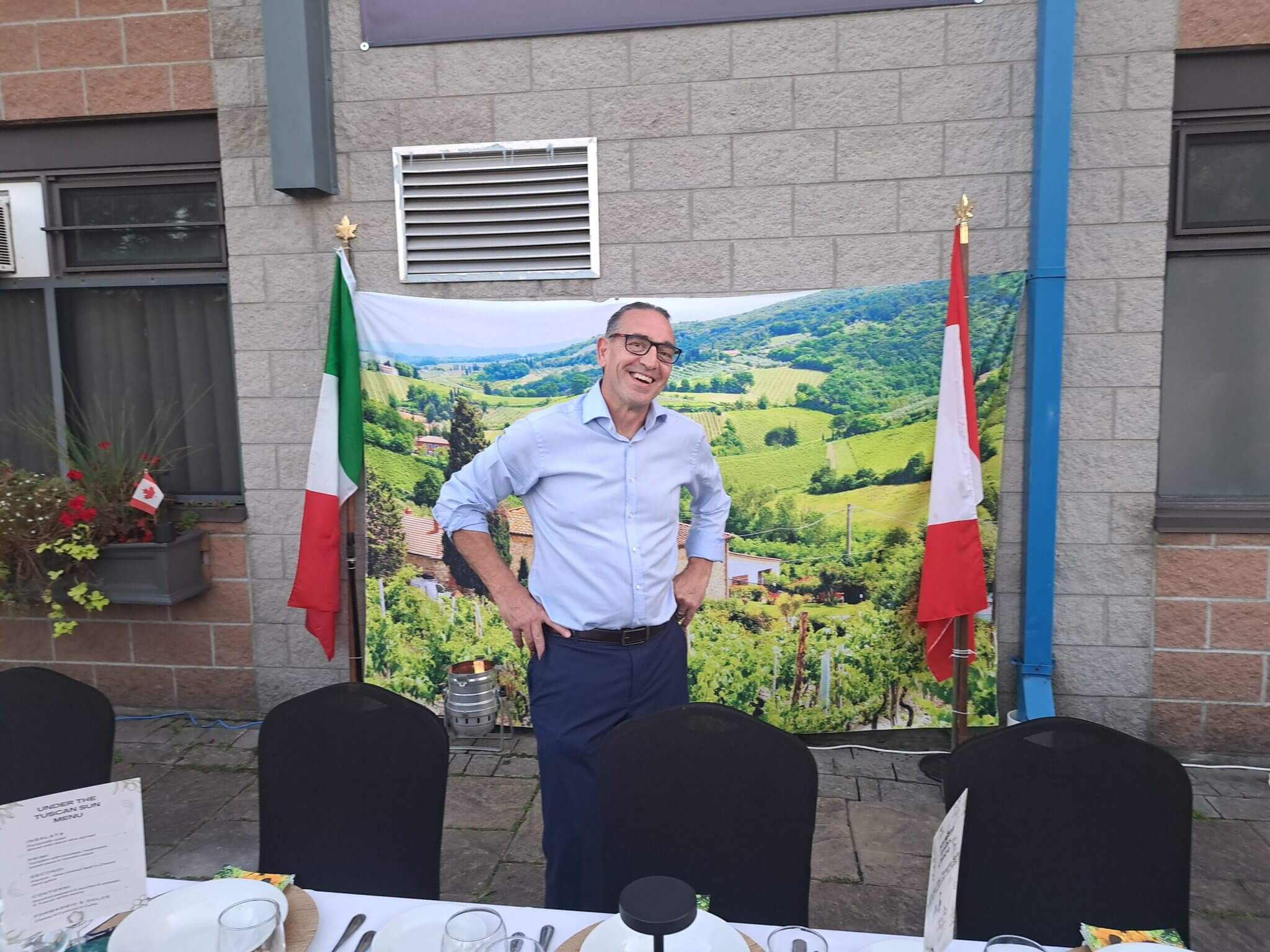 Man standing in front of a scenic countryside backdrop between two flags.