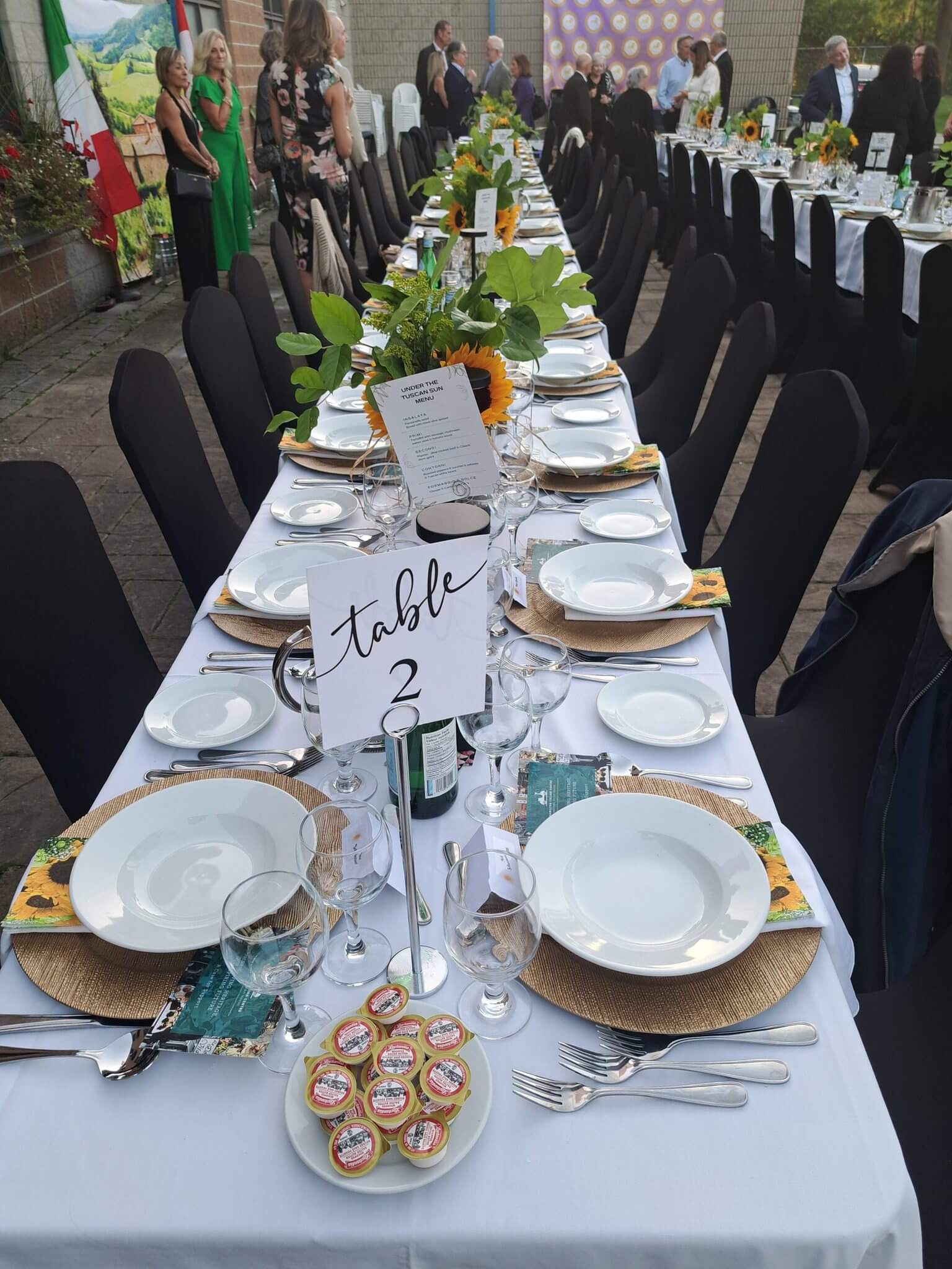 Elegantly set banquet table with white plates, gold chargers, and black chair covers.