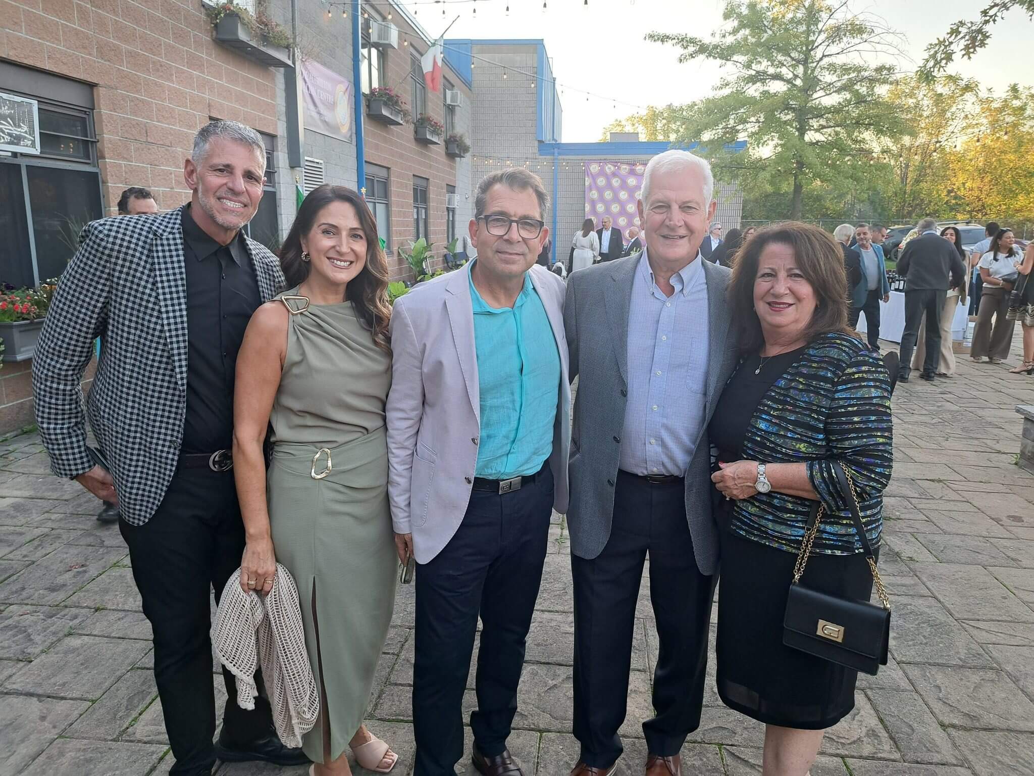 Five people standing together outdoors, dressed in semi-formal attire, smiling at the camera.