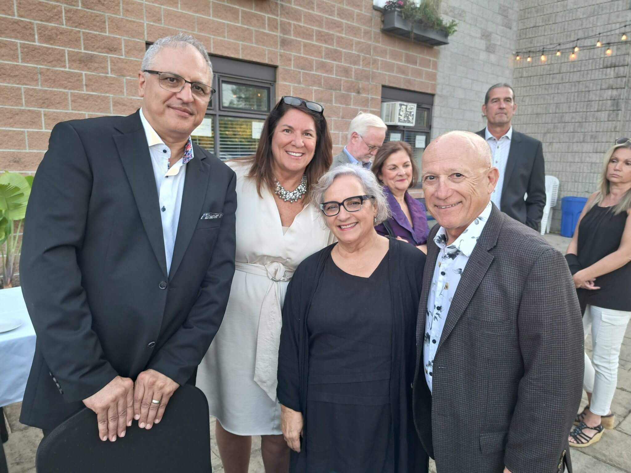 Five smiling adults dressed in formal attire pose outdoors.