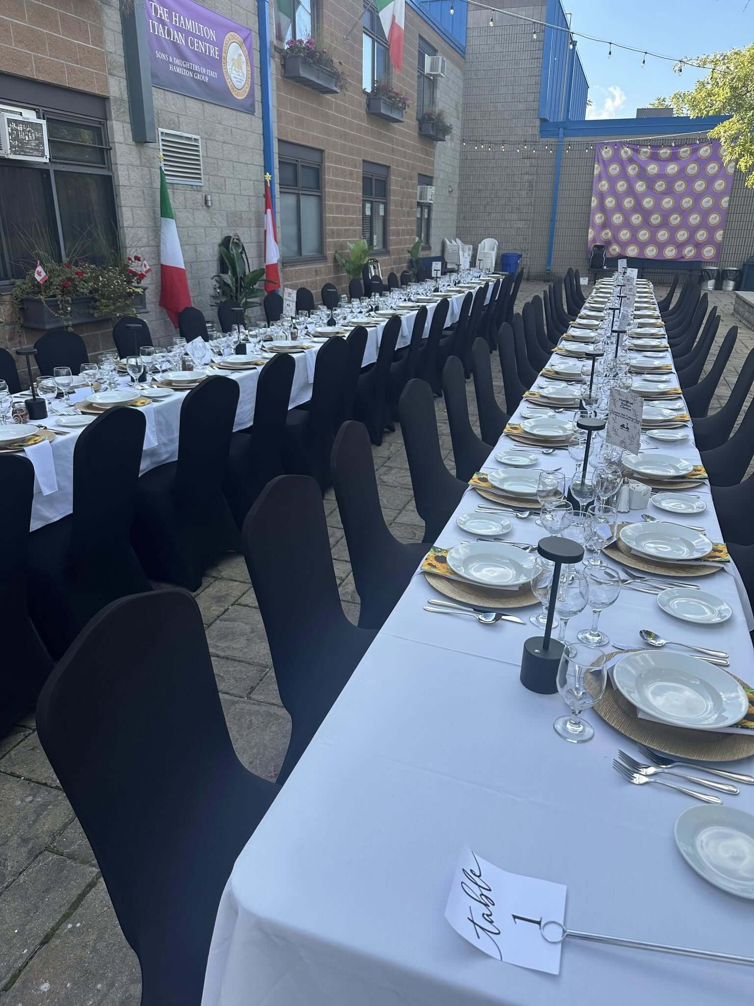 Elegant long table set for an outdoor formal event with white tablecloth and black chairs.