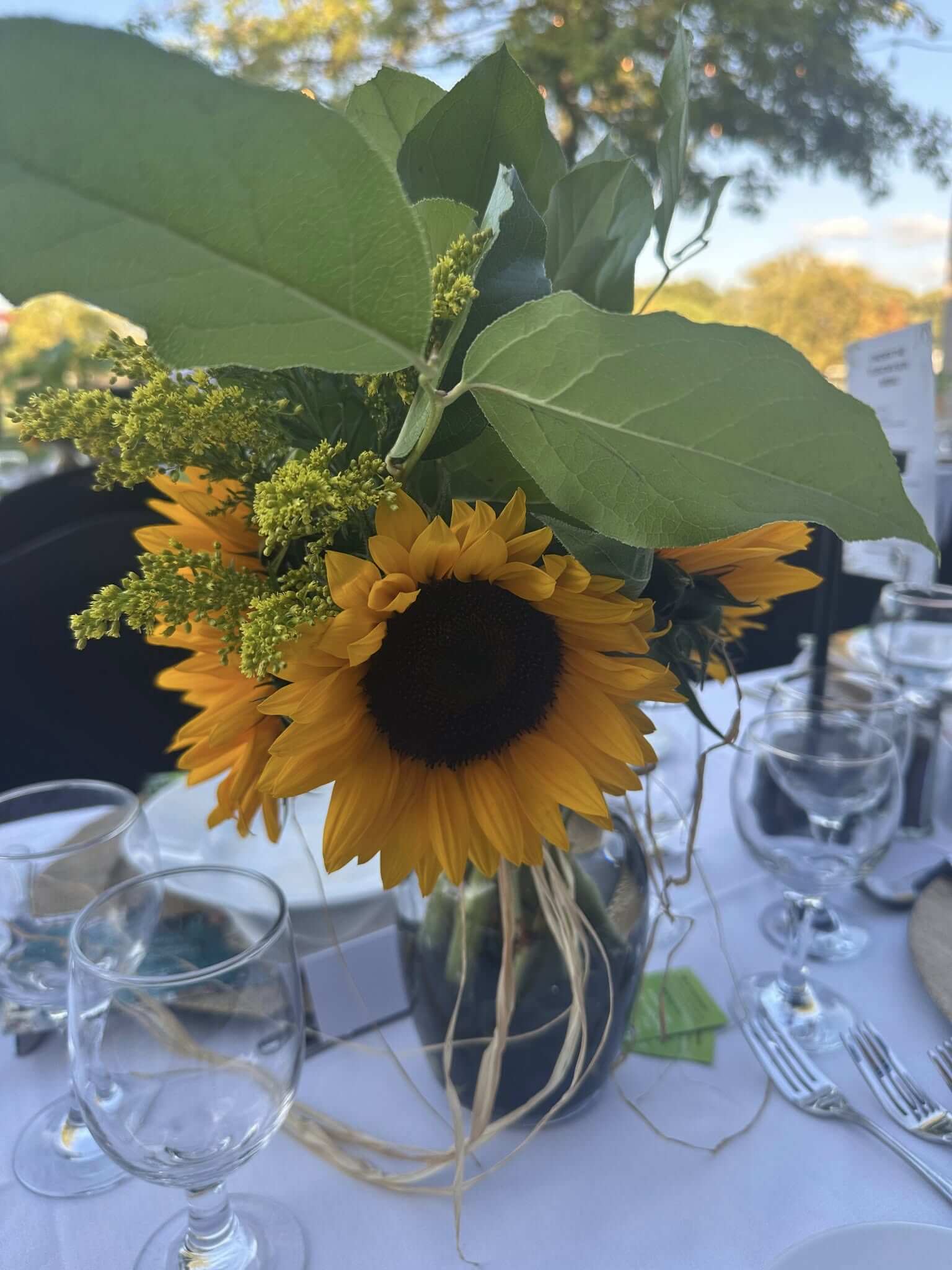 A sunflower centerpiece in a glass jar on a dining table.
