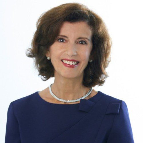 Professional portrait of a smiling woman in a navy blue dress and pearl necklace.
