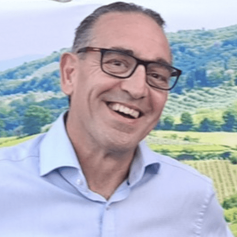 Smiling man wearing glasses and a light blue shirt outdoors.